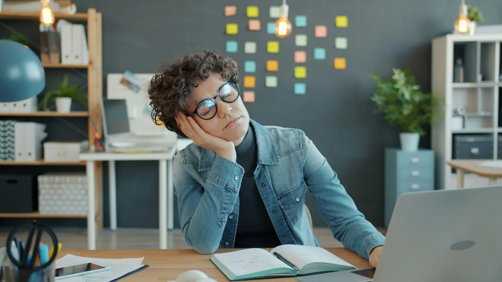 A tired worker resting their head on one hand at a desk.