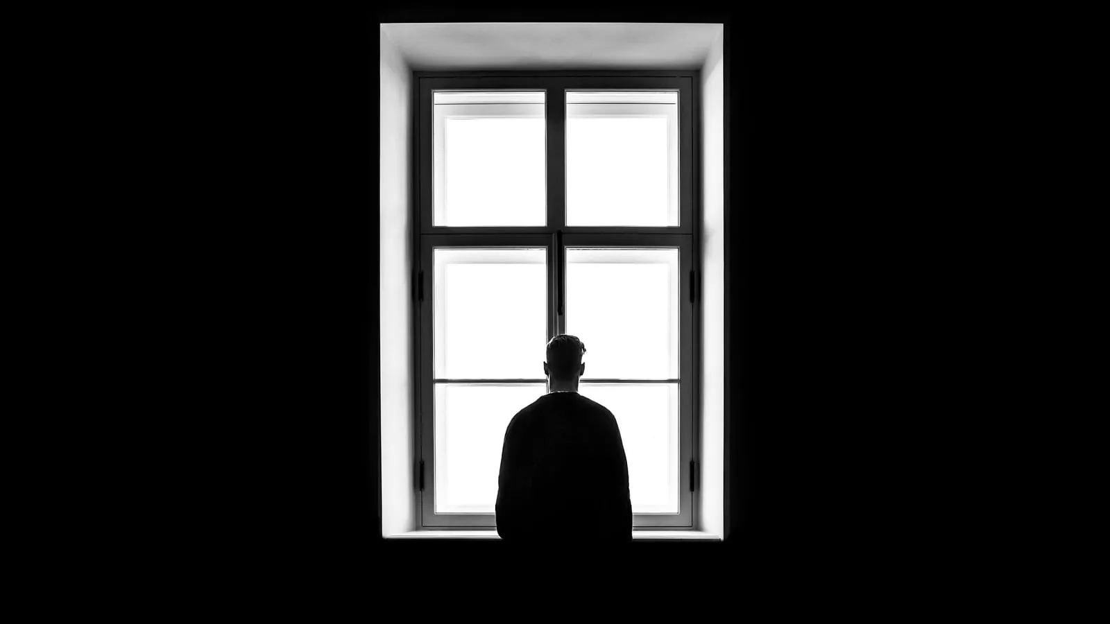 A person standing alone in front of a bright window.