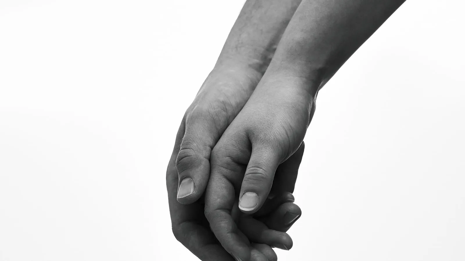 Two people holding hands against a soft white background, a simple gesture of human connection.