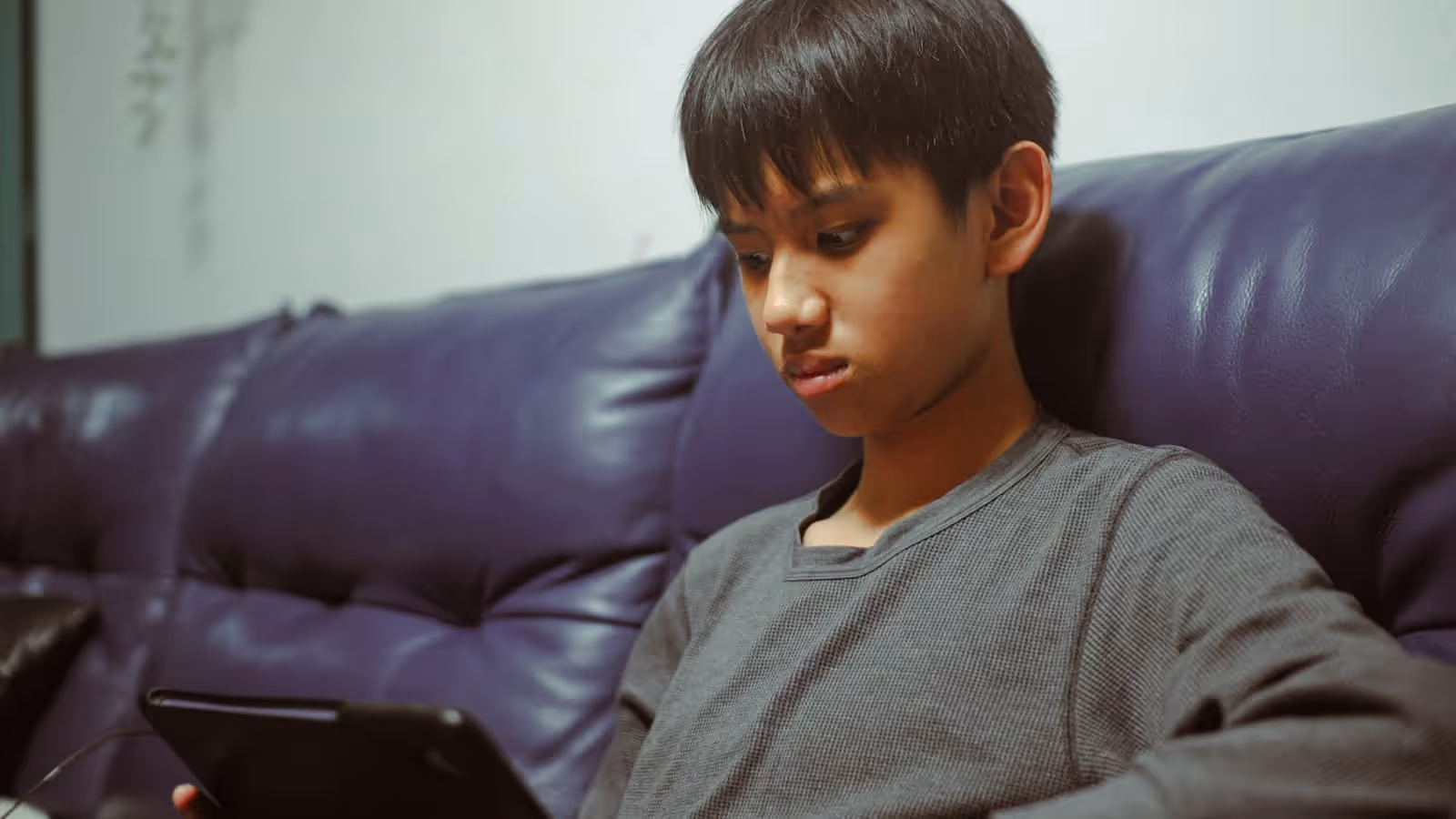 Un niño sentado en un sofá, mirando hacia abajo a una tableta que sostiene en su regazo.