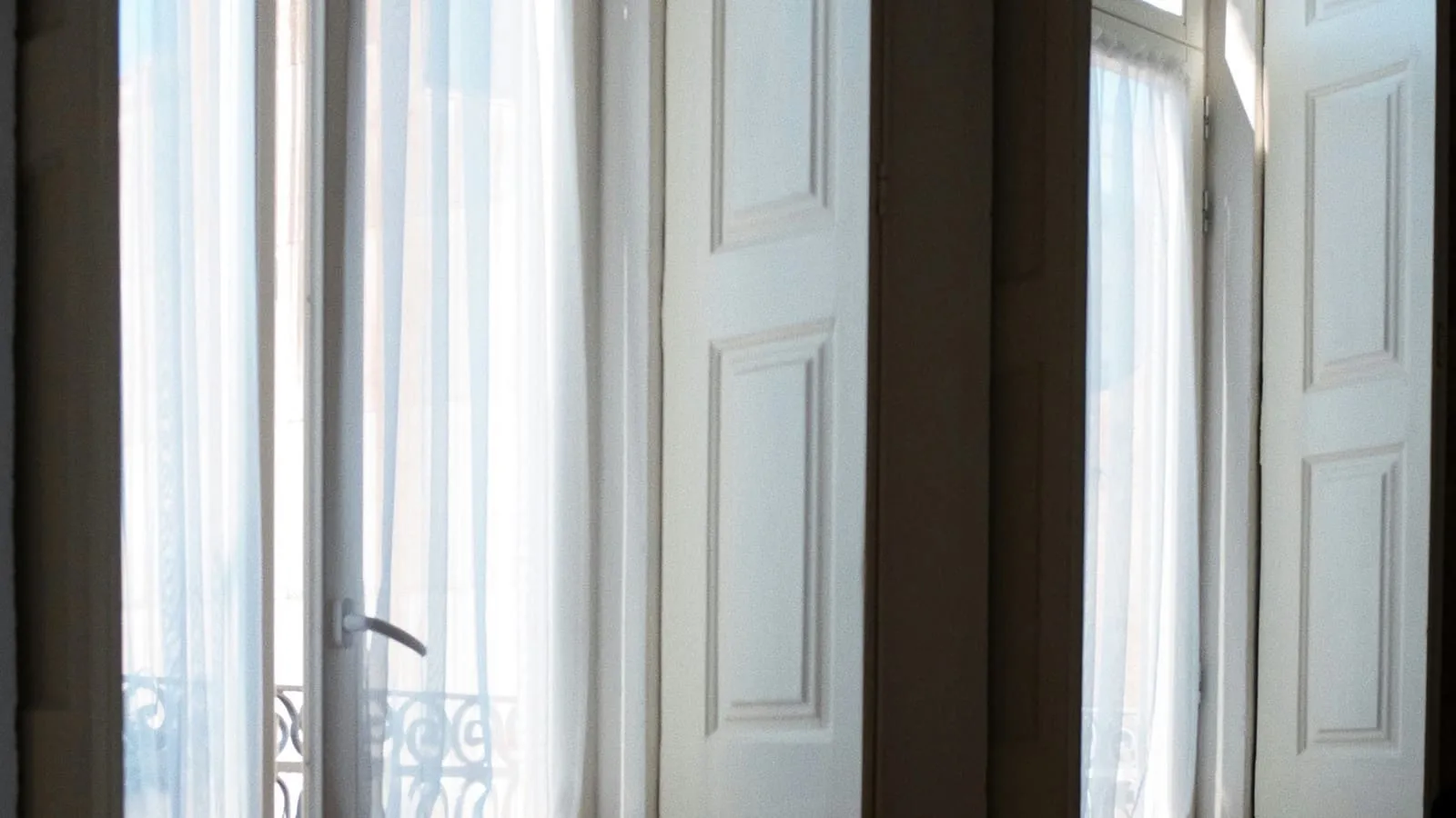 Soft morning light through bedroom windows over white bedding.