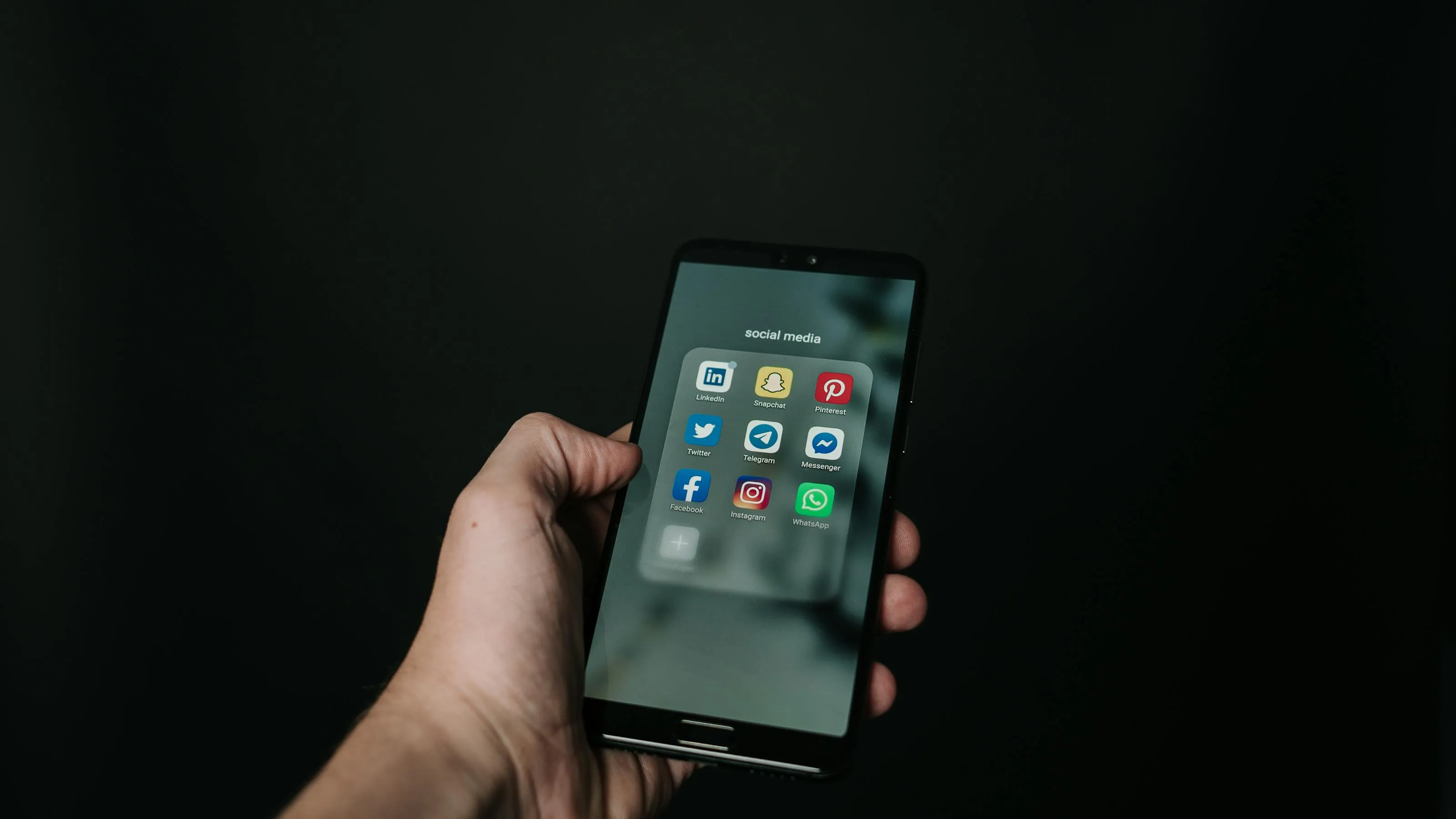 Hand holding a smartphone with bright social media app icons reflected on the screen against a soft blurred background.