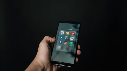 Hand holding a smartphone with bright social media app icons reflected on the screen against a soft blurred background.