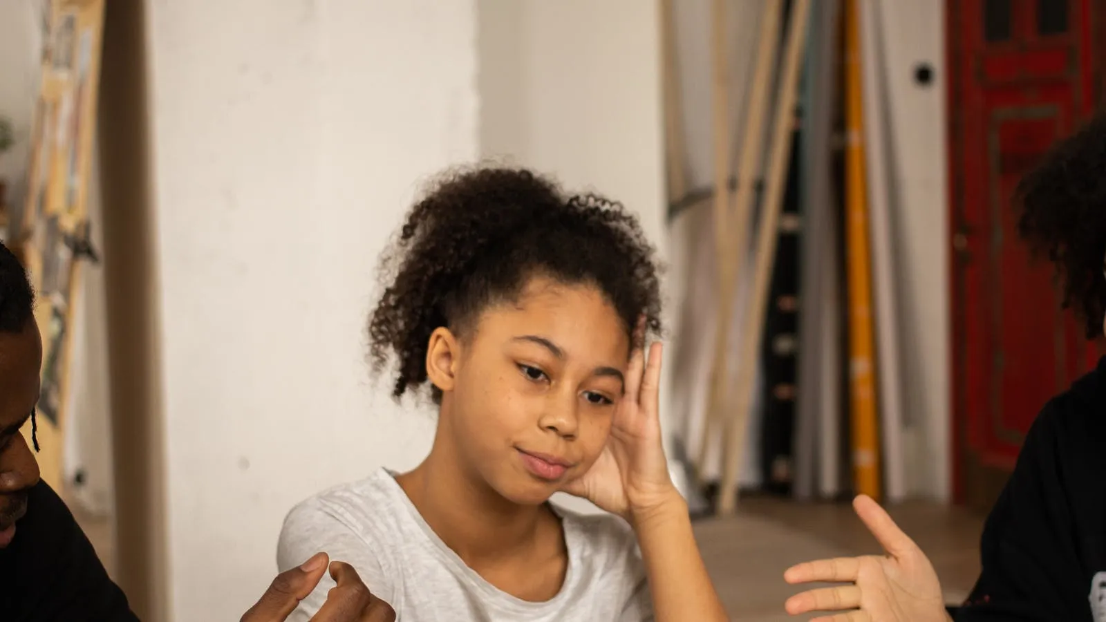 Teenage girl in a hoodie looking down at a phone, soft window light behind her.