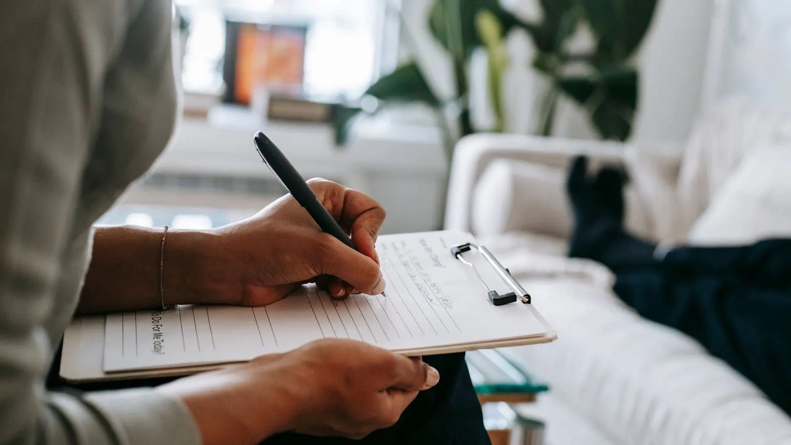Therapist's notebook and a small leafy plant on a wooden desk in a calm, warmly lit room.