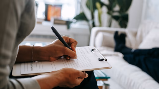 Therapist's notebook and a small leafy plant on a wooden desk in a calm, warmly lit room.