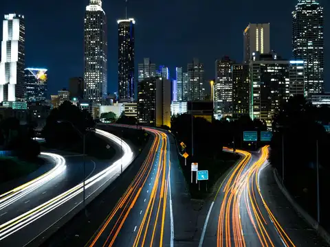 The downtown Atlanta skyline at night seen from the Jackson Street Bridge, with long light trails from traffic on the freeway below.