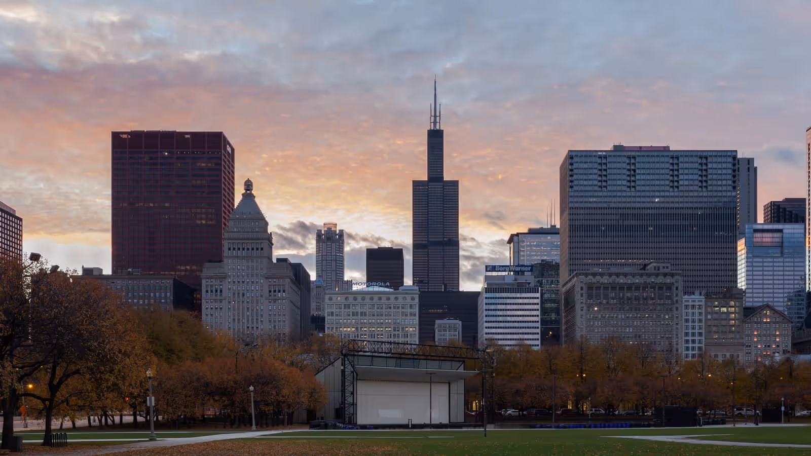 Die Skyline von Chicago bei Dämmerung, gesehen über den Grant Park, mit dem Willis Tower und seinen Antennen im Zentrum und herbstlichen Bäumen im Vordergrund.