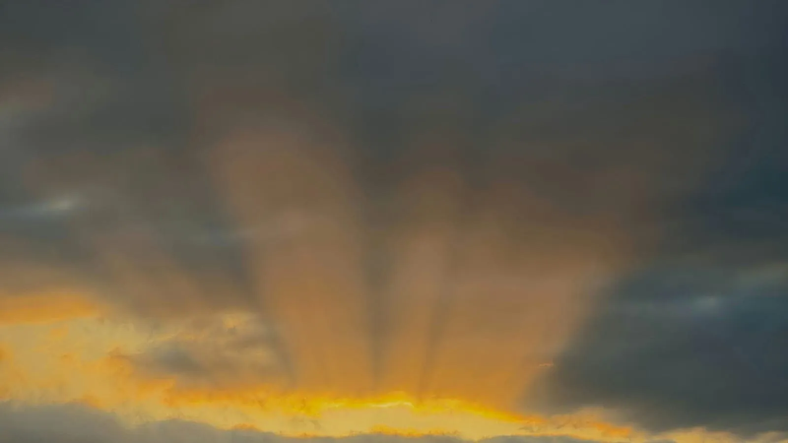 Soft sunlight breaking through heavy clouds over an open road, suggesting hope after difficulty.